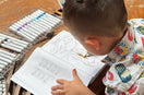 Child coloring a Bat from Animals, Insects and Ocean Friends Coloring Book for children on wooden table.
