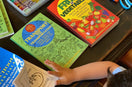 Child using Ermenrich Designs activity coloring books with crayons, glue, and scissors on table