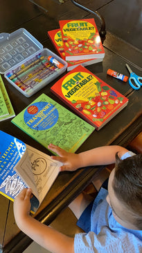 Child using Ermenrich Designs activity coloring books with crayons, glue, and scissors on table