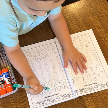 Child tracing lines inside Preschool Essentials coloring book for kids by Ermenrich Designs