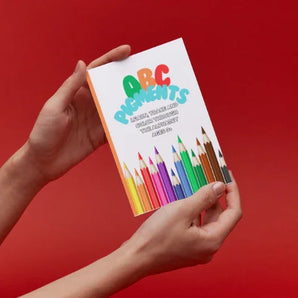 Hands holding Ermenrich Designs ABC Placements educational coloring book with colored pencils cover