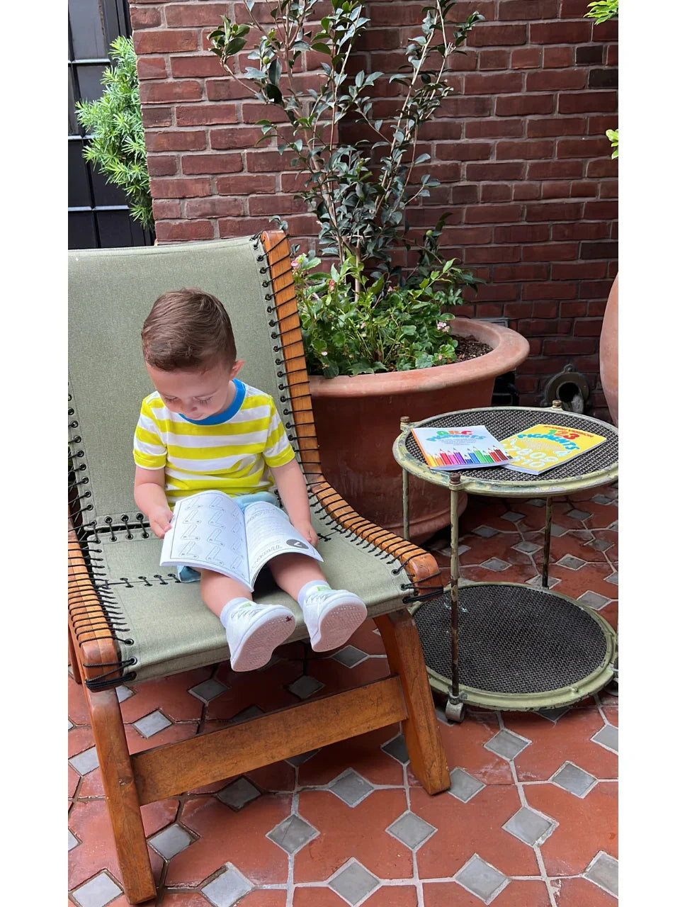 Toddler reading 123 Pigments: Spanish version coloring book by Ermenrich Designs. educational coloring book outdoors on lounge chair
