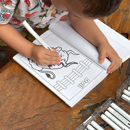 A child coloring the Bull coloring page from Animals, Insects and Ocean Friends Coloring Book from Ermenrich Designs on wooden table.