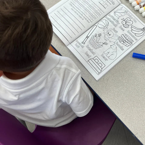 Child using Ermenrich Designs alphabet activity coloring book at a classroom table with markers.