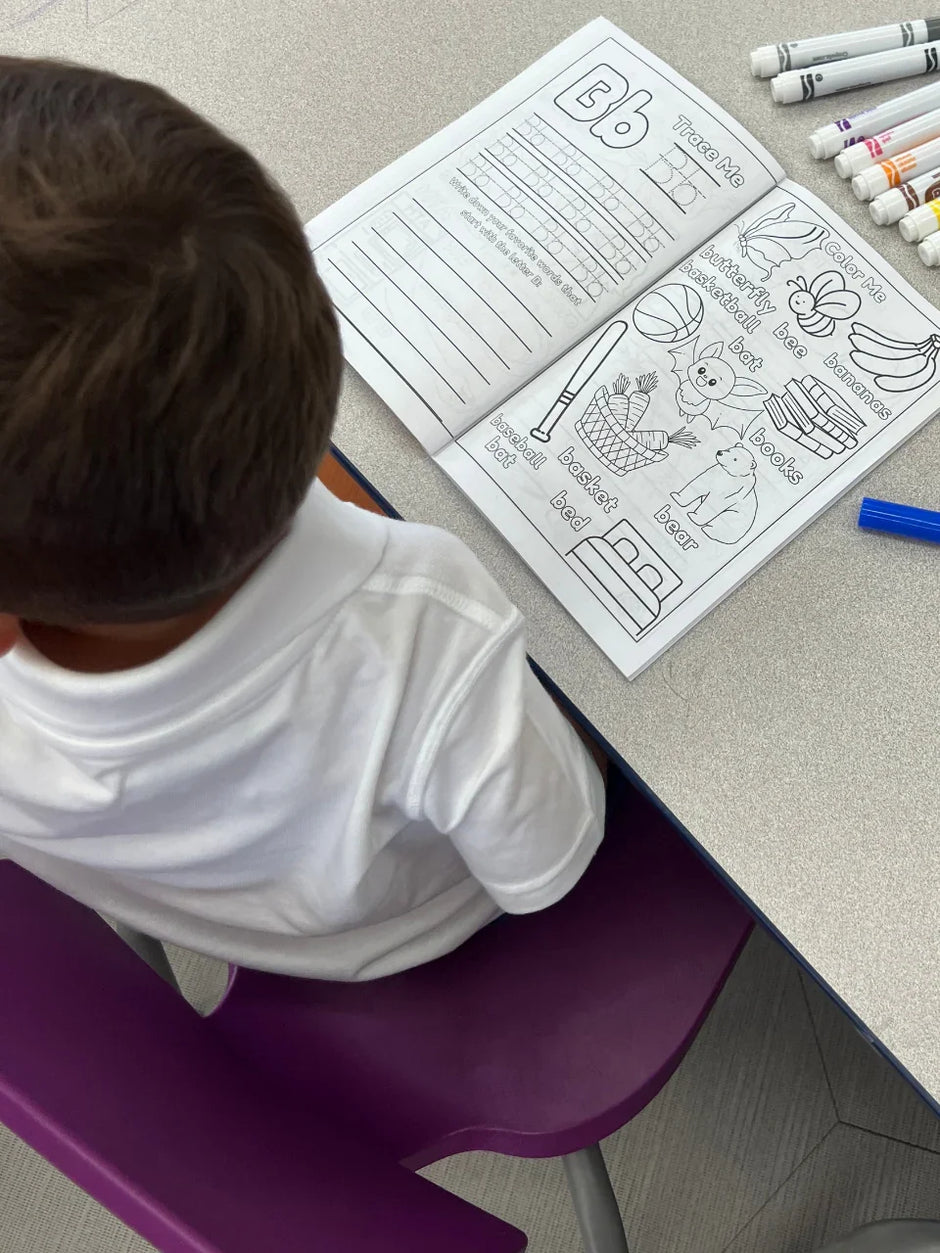 Toddler sitting on chair with ABC Pigments coloring book open to lette B activity tracing, spelling and coloring pages.