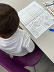 Toddler sitting on chair with ABC Pigments coloring book open to lette B activity tracing, spelling and coloring pages.