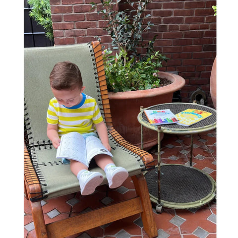 Toddler reading Ermenrich Designs educational coloring book outdoors on lounge chair